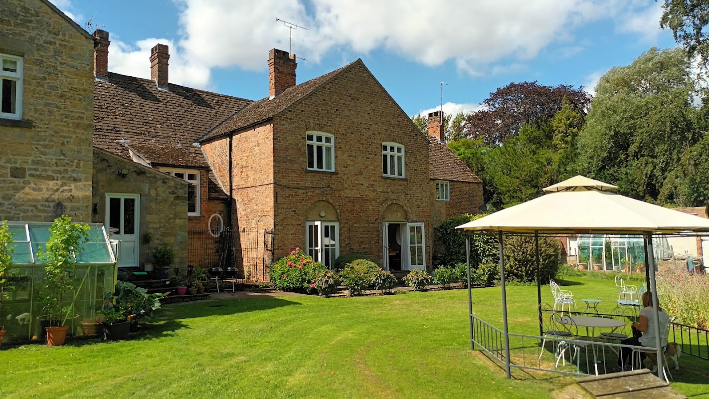Newburgh House features a brick exterior, manicured lawn, garden plants, and a gazebo with seating in a serene setting.