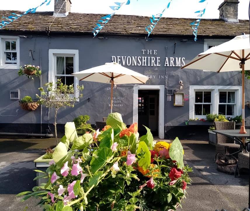 The Devonshire Arms restaurant features a grey exterior, outdoor seating, umbrellas, and vibrant flower arrangements.