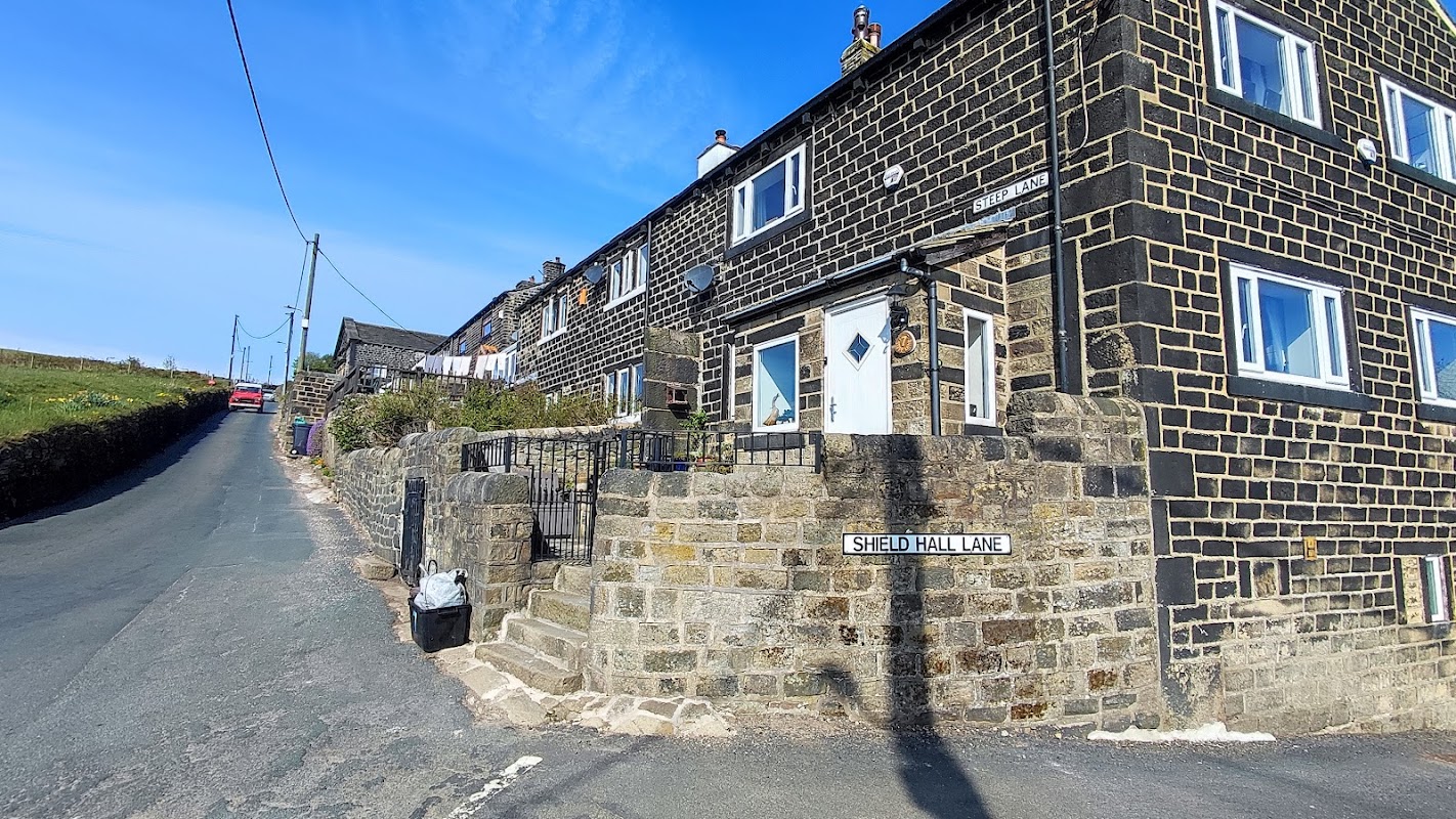 Aarons Campsite features a stone building with a sign on Shield Hall Lane, surrounded by greenery and a clear blue sky.