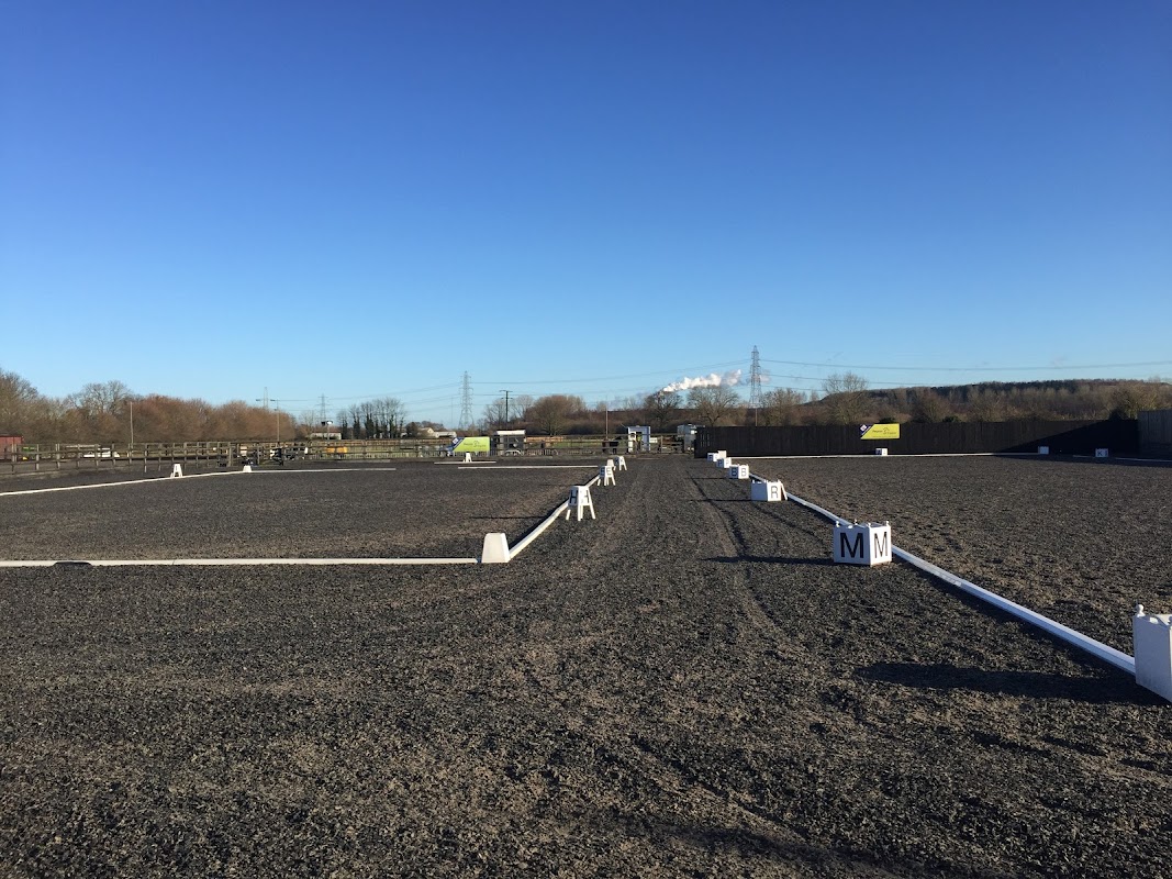 Wide view of a dressage arena with white markers, surrounded by a clear blue sky and distant hills in Yorkshire.