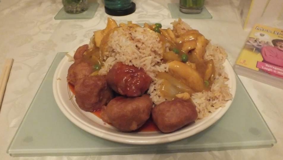 Plate of rice with chicken, peas, and sweet and sour meatballs, set on a table with chopsticks and green drinks.