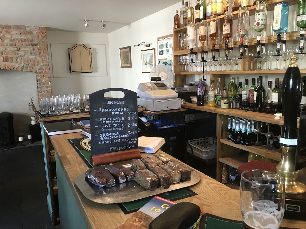 Bar counter with a variety of drinks, glassware, a chalkboard menu, and a platter of snacks in a cozy setting.