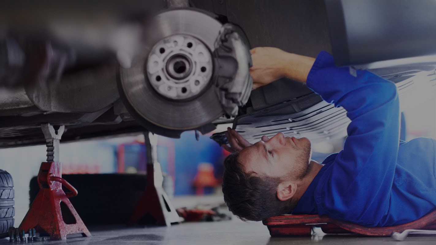 A mechanic in blue coveralls working under a car, focusing on the brake assembly in a garage setting.