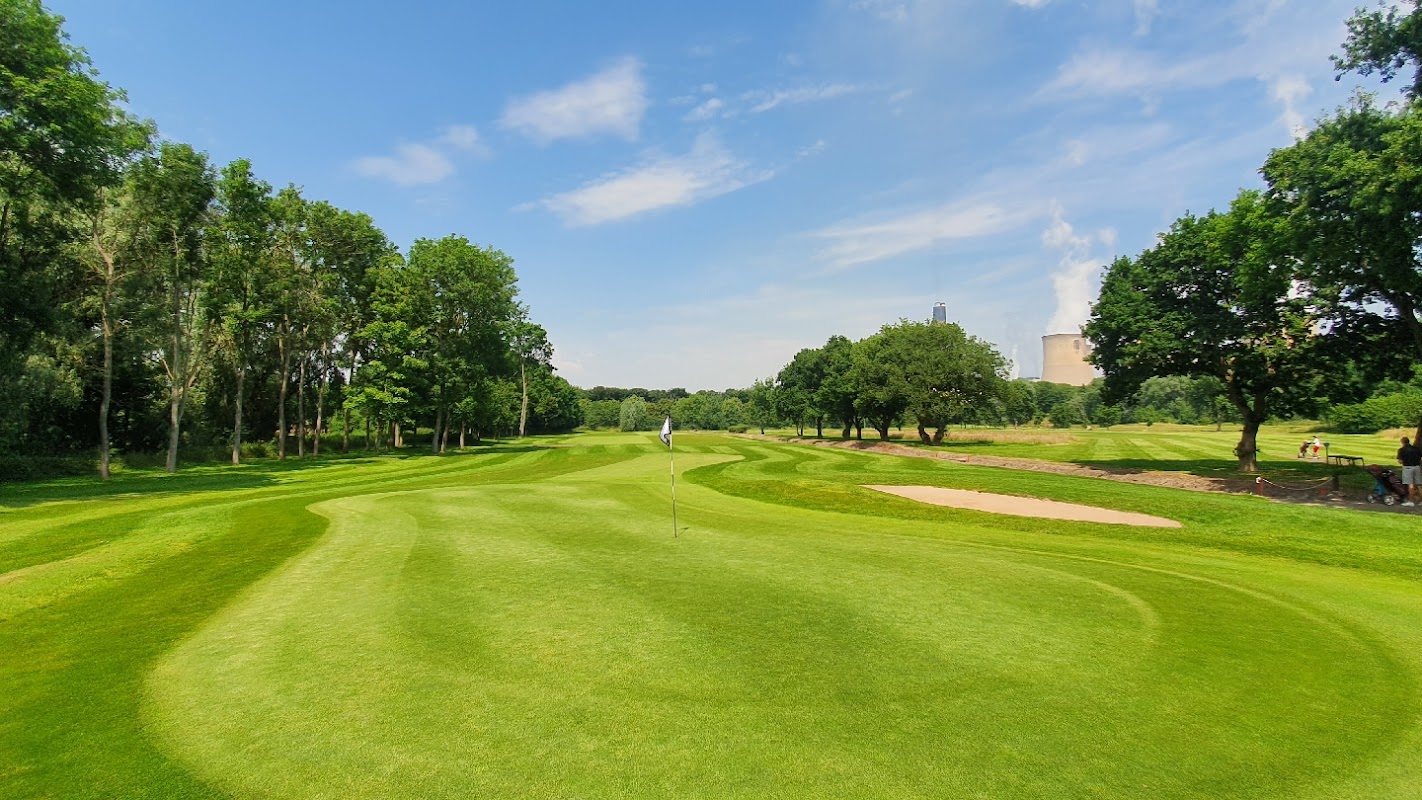 Lush green golf course with rolling fairways, trees, and a sand trap under a clear blue sky in Drax, North Yorkshire.