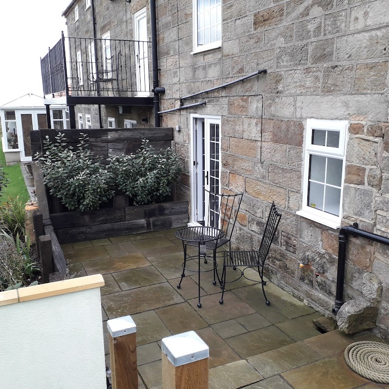 Stone exterior of Alum House with a small patio, black metal table and chairs, and greenery in planters.