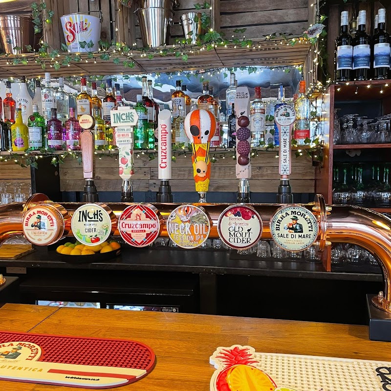 Colorful beer taps lined up on a wooden bar, with various brands and drinks visible, surrounded by bottles and festive decor.