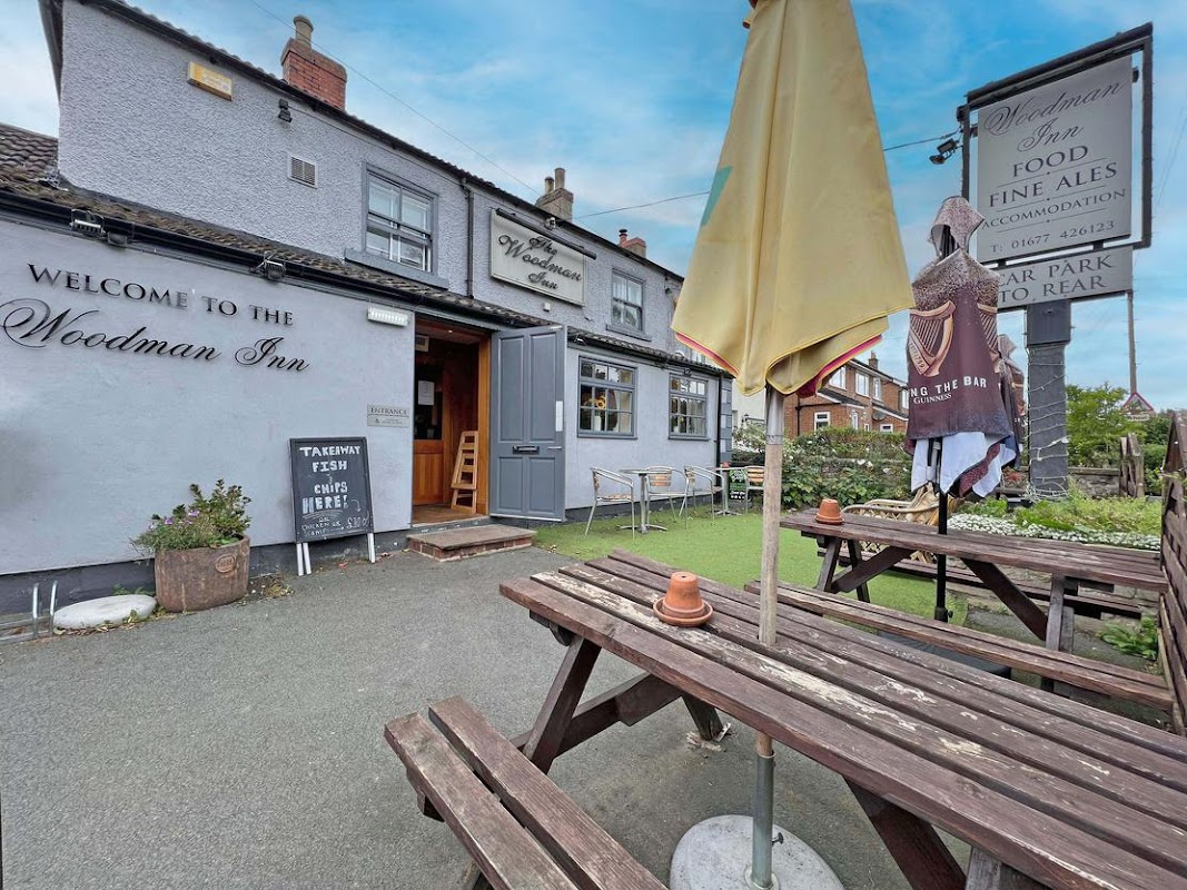 Welcome to The Woodman Inn, featuring outdoor seating, a yellow umbrella, and a sign for food and fine ales.