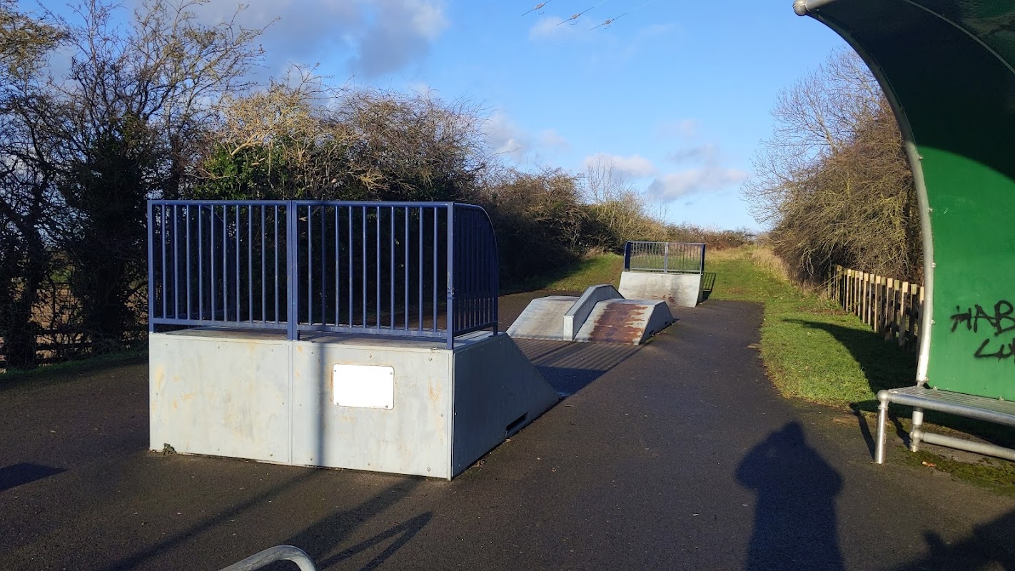 Skatepark ramps with blue railings, surrounded by greenery and a clear blue sky in Fairburn, North Yorkshire.