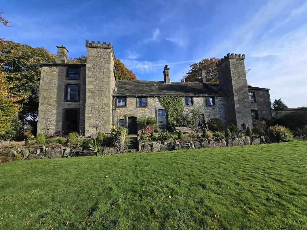 Historic stone building with towers, surrounded by lush greenery and colorful foliage under a bright blue sky.