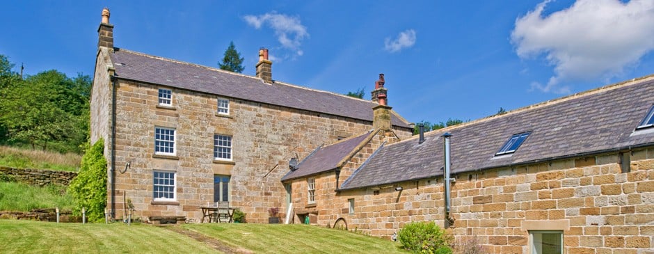 Historic stone cottages in Castleton, Yorkshire, surrounded by lush greenery under a bright blue sky.