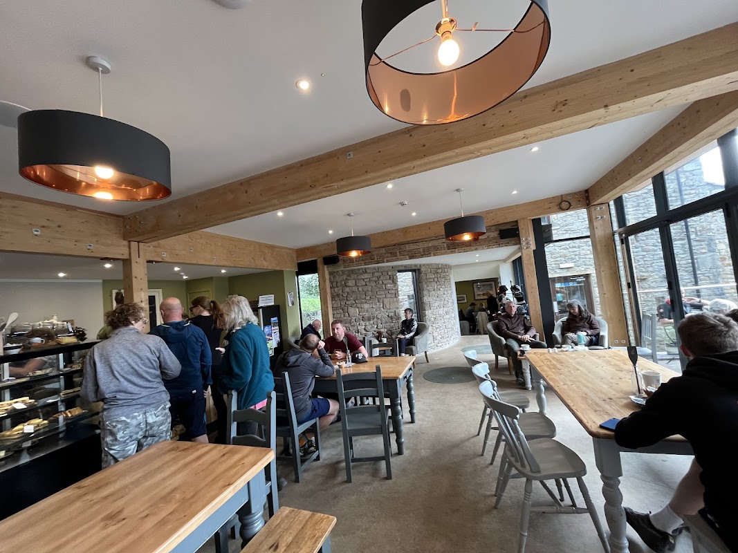 Modern café interior with wooden beams, tables, and customers enjoying food and drinks in a cozy atmosphere.