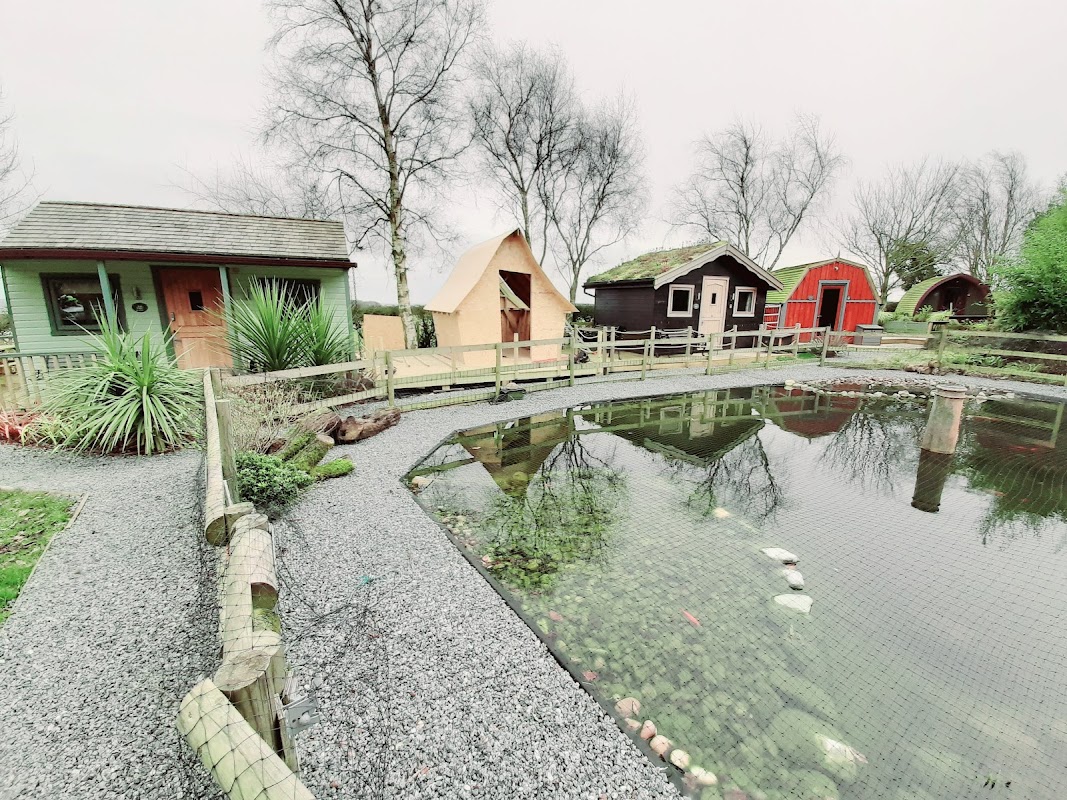 Glamping cabins and a pond surrounded by gravel paths and greenery at Seaways Glamping and Camping in Yorkshire.