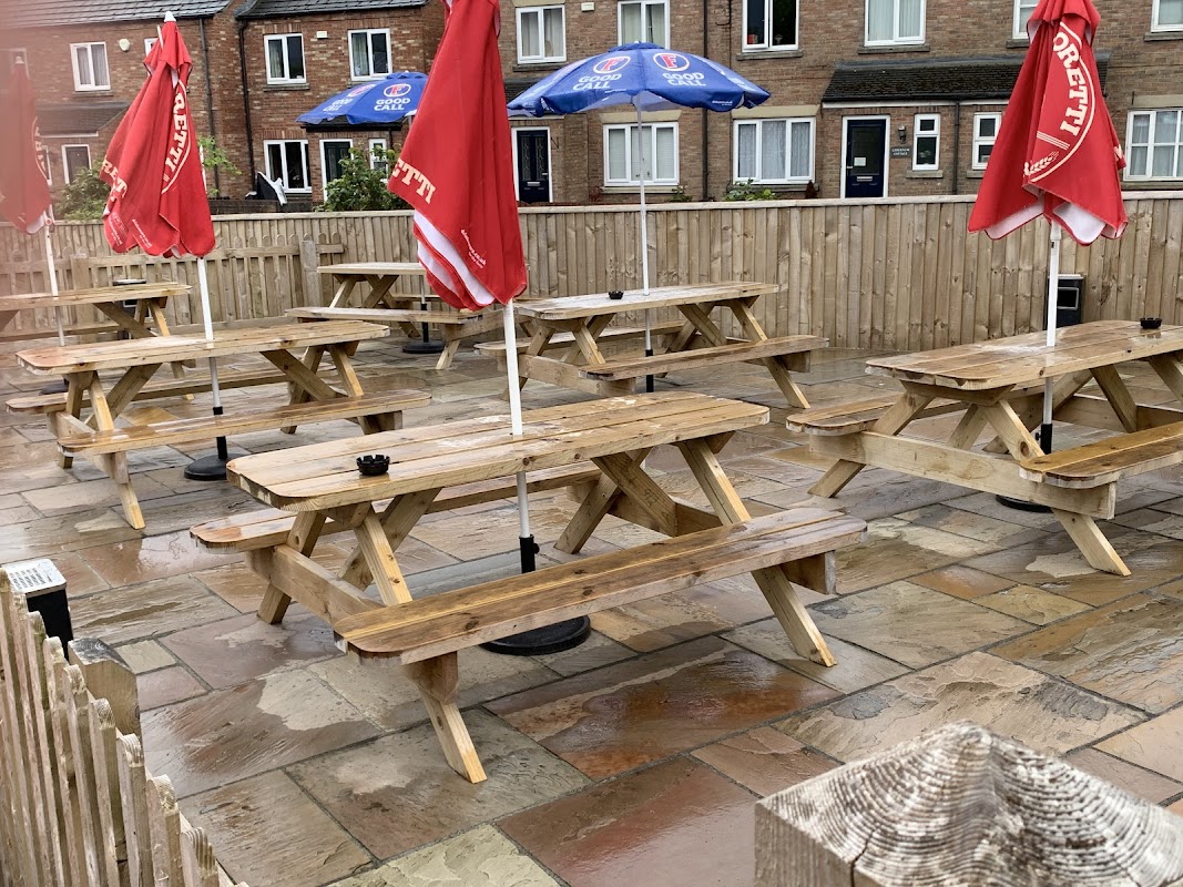 Outdoor seating area with wooden picnic tables, red umbrellas, and a stone patio at The Manor Inn in Fridaythorpe.