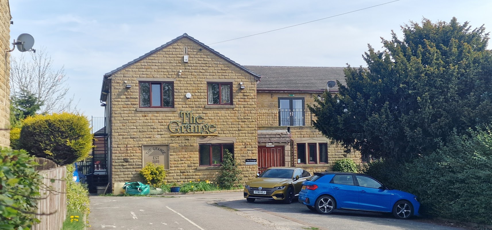 The Grange bar features a stone exterior, green shrubs, and parked blue cars in a sunny Yorkshire setting.