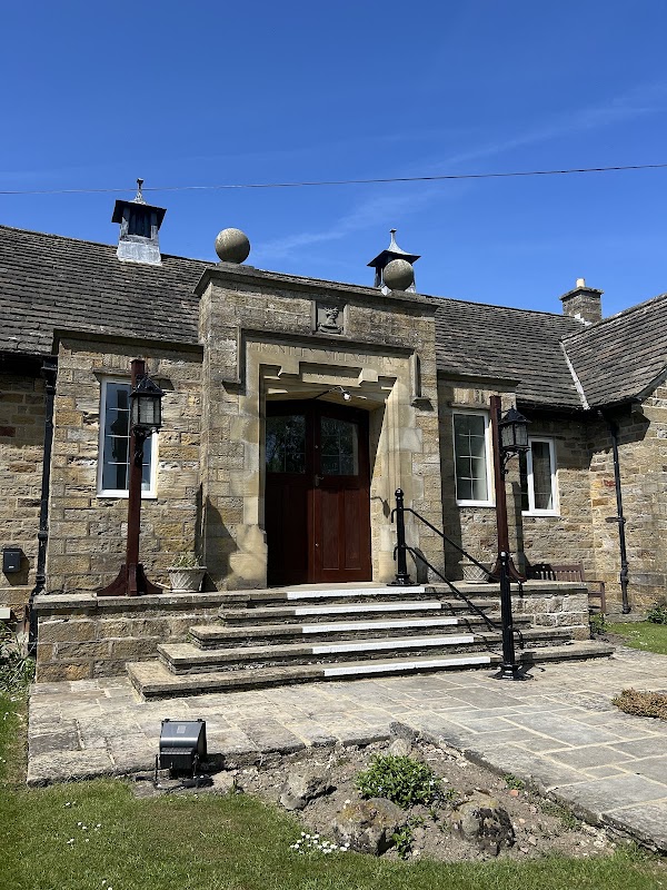 Stone entrance with steps, decorative lanterns, and a clear blue sky above Grantley Village Hall in Yorkshire.
