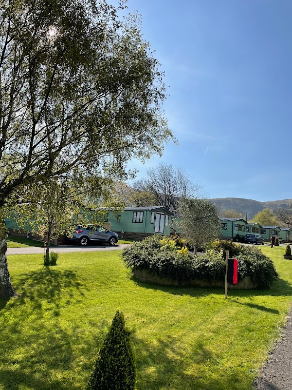 Lush green lawn with holiday caravans, trees, and a clear blue sky at Toft Hill Country Holiday Park in North Yorkshire.