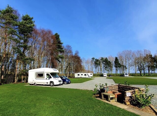 Campsite with caravans and motorhomes, surrounded by trees and a clear blue sky in Great Hatfield, Yorkshire.
