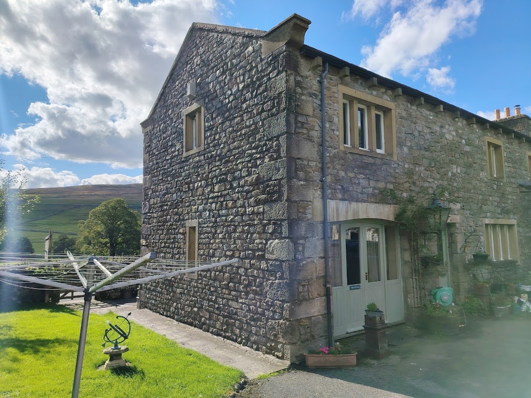 Stone cottage in Halton Gill, Yorkshire, with a garden, washing line, and scenic hills in the background under a blue sky.