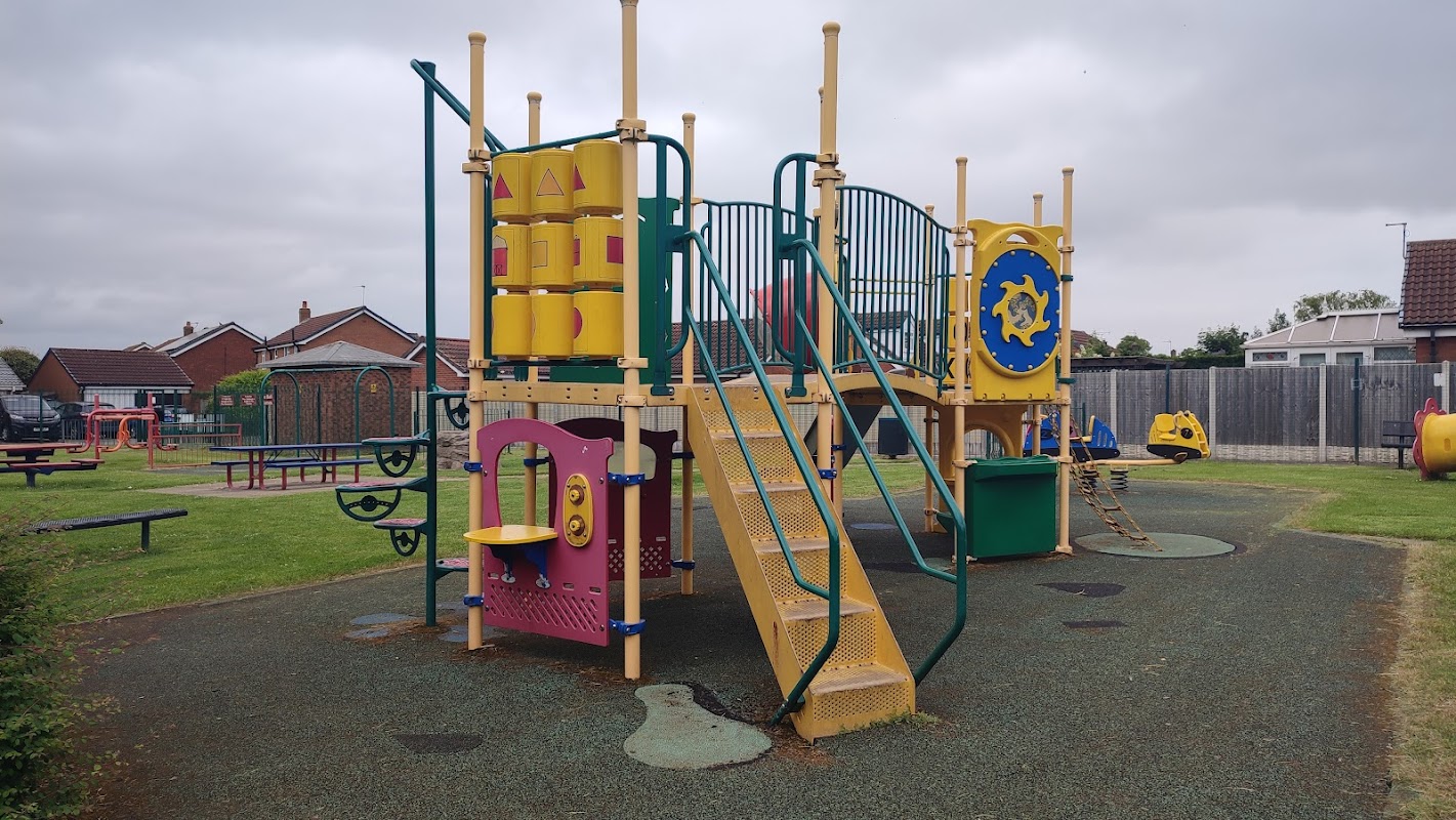 Colorful playground equipment with slides, climbing structures, and play panels set in a grassy area.