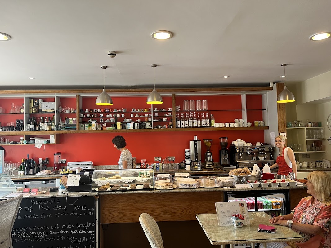 Bright coffee shop interior with a red wall, glass display of pastries, and two women chatting near the counter.