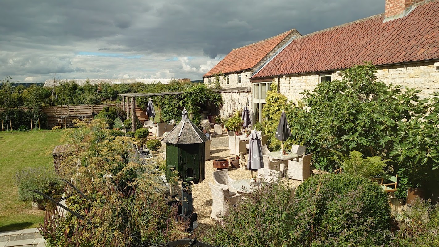Charming lodge surrounded by greenery, outdoor seating, and a rustic stone building under a cloudy sky.