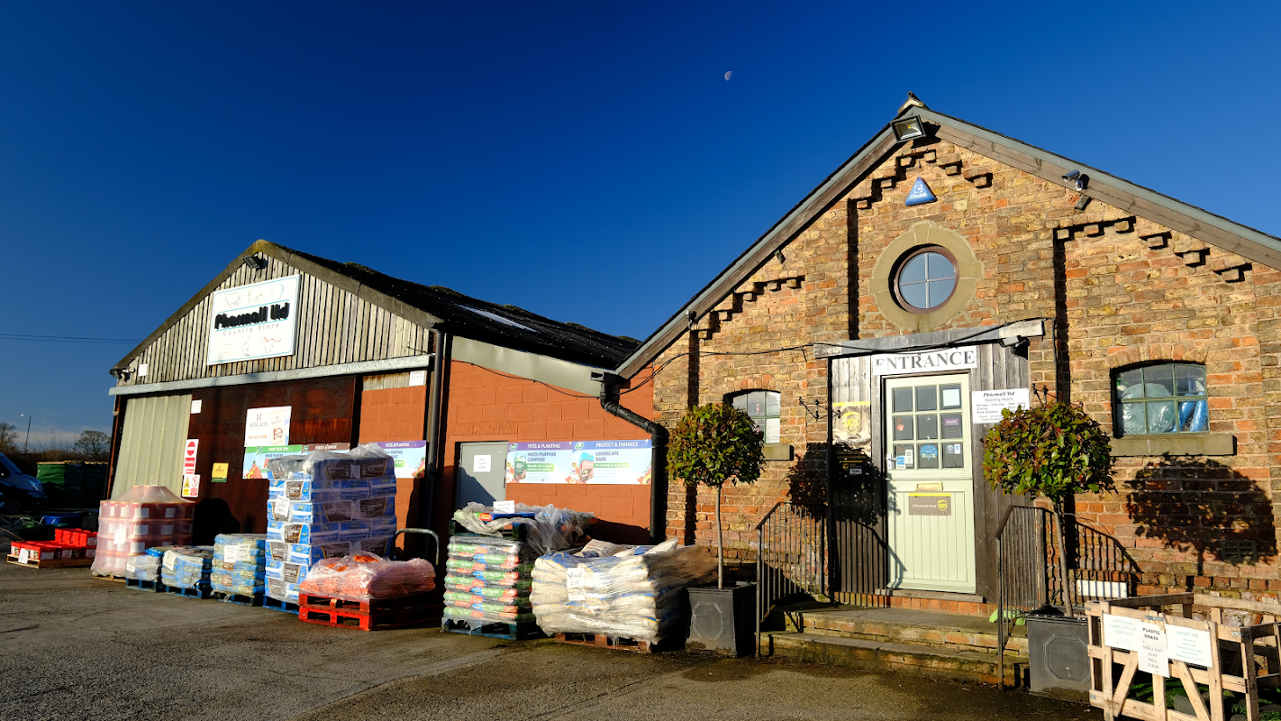 Pharmall Country Store features a brick building with a green entrance, stacked bags, and a clear blue sky.