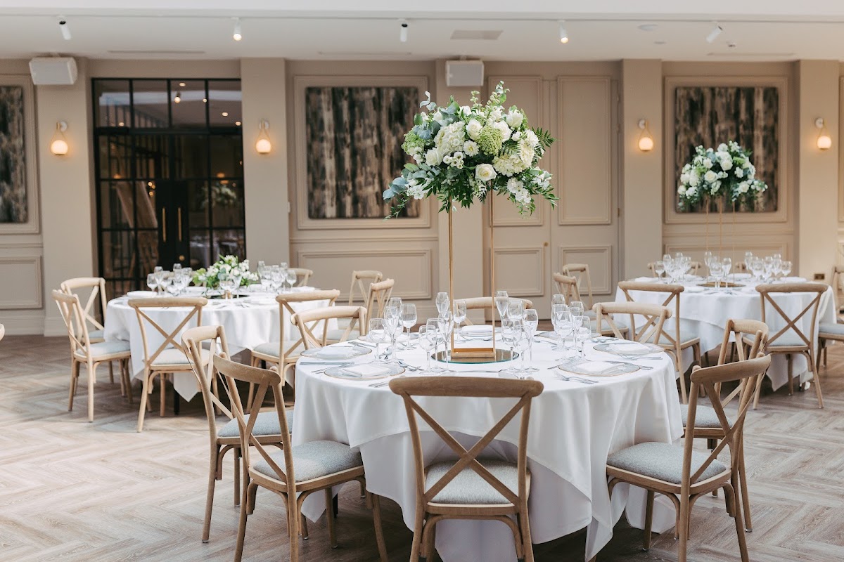 Elegant dining setup with round tables, white tablecloths, and tall floral centerpieces in a stylish venue.