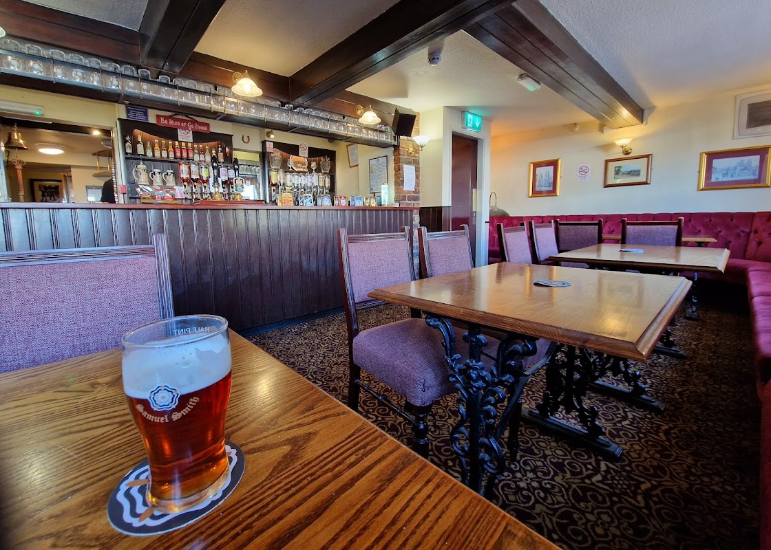 Cozy bar interior with wooden tables, chairs, a counter with drinks, and a pint of beer on a table.