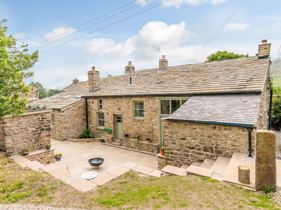 Stone farmhouse with a slate roof, surrounded by greenery and a stone patio, located in a rural Yorkshire setting.