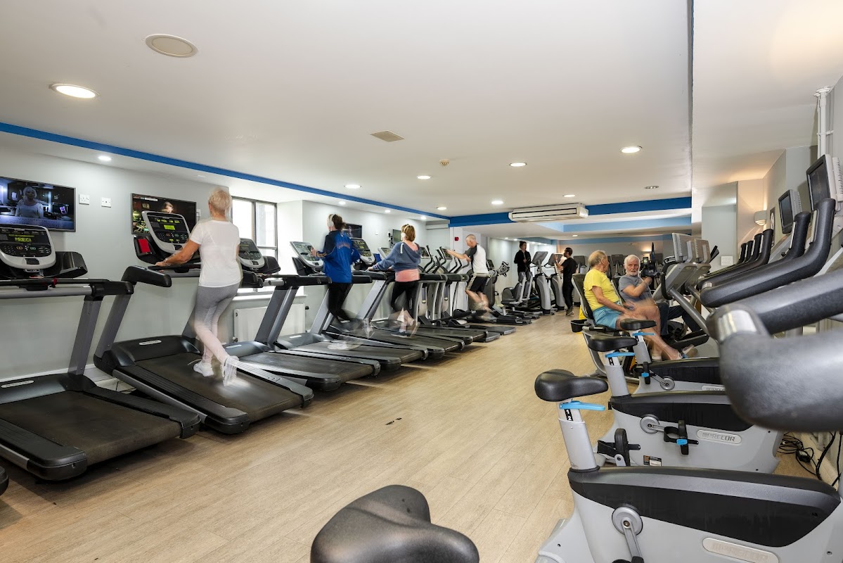 Fitness enthusiasts using treadmills and exercise bikes in a bright gym with modern equipment and large windows.