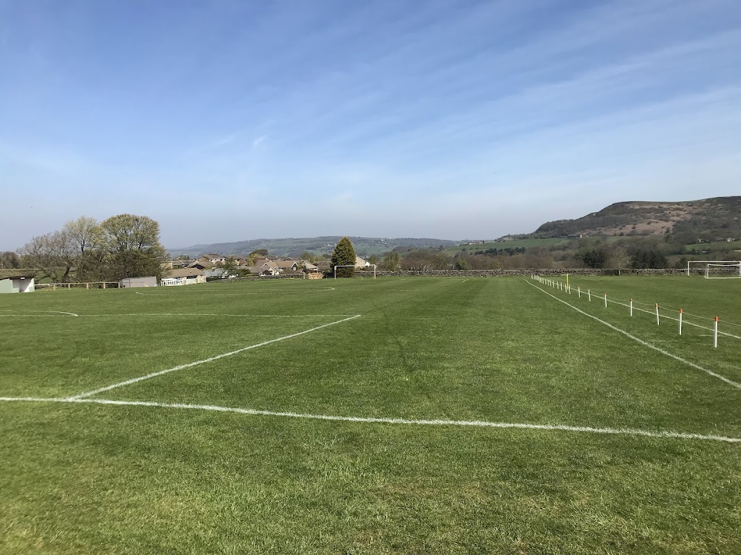 Green football pitch with goalposts, surrounded by trees and hills under a clear blue sky in Hepworth, Yorkshire.