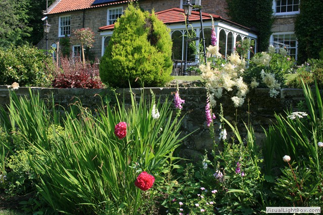 Charming garden with colorful flowers in front of a brick house at High Dalby House, Dalby Forest, Yorkshire.