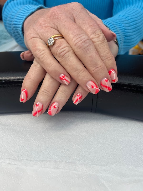 Hands with beautifully manicured nails featuring red and white heart designs, resting on a black surface.