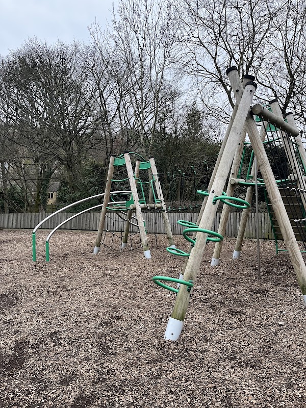 Playground equipment with climbing frame and slide, surrounded by wood chips and trees in a park setting.