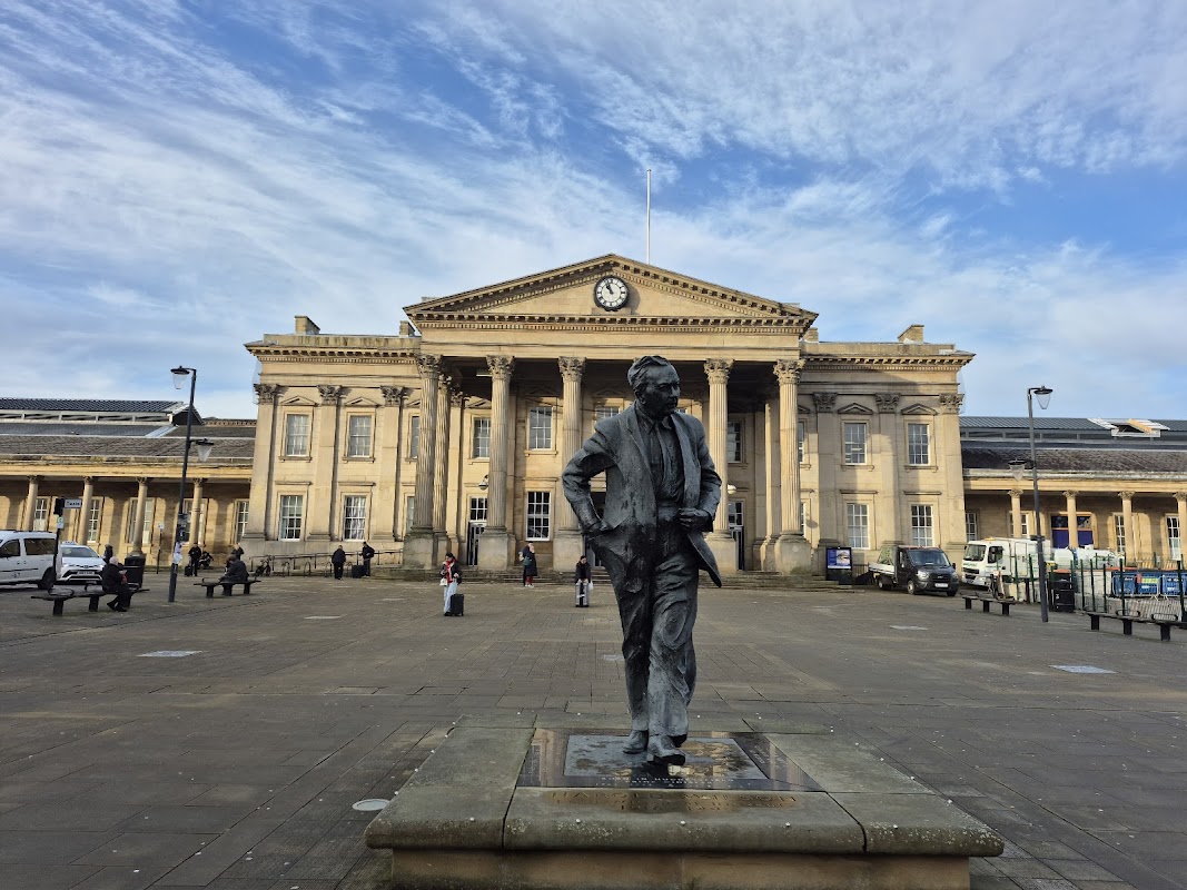 Statue in foreground with a historic building featuring columns and a clock in the background under a blue sky.