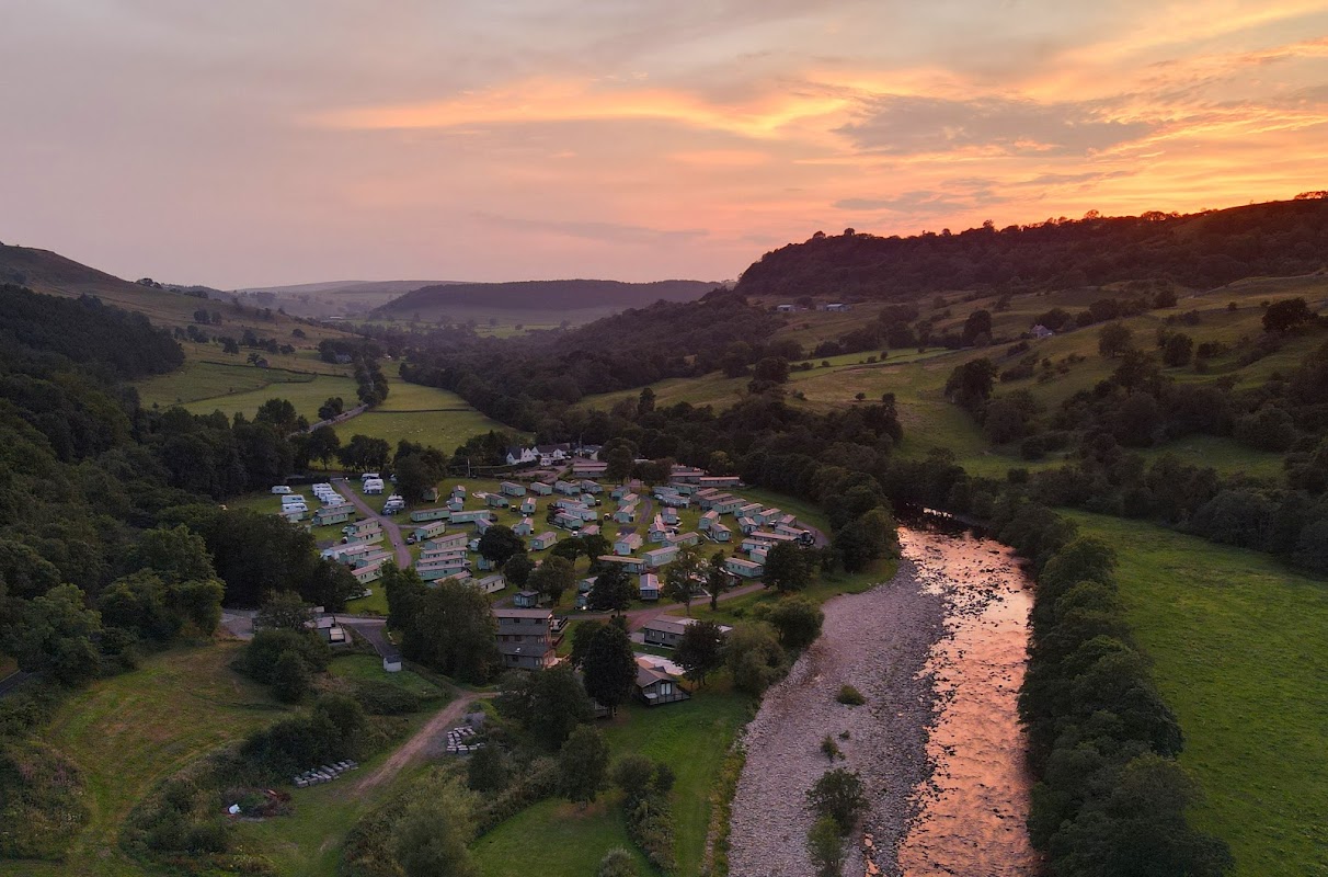Aerial view of Swale View Caravan Park at sunset, surrounded by lush hills and a flowing river.