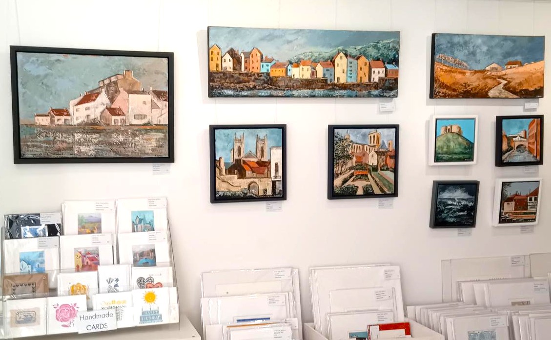 Art gallery wall with colorful landscape paintings and greeting cards display