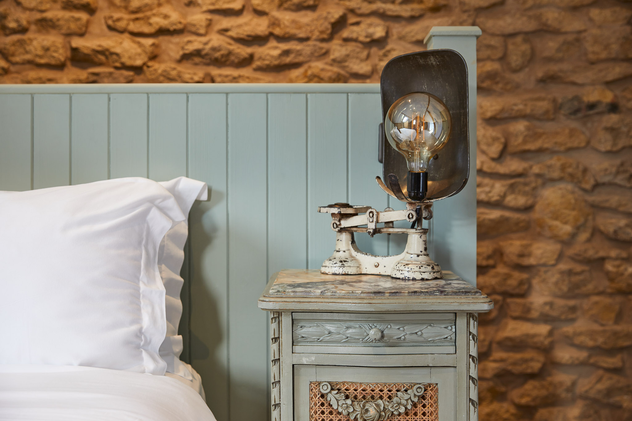 Rustic bedroom with stone walls, vintage scale lamp, and elegant bedding
