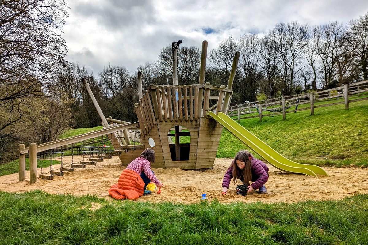 Wooden playground with ship structure and slide surrounded by trees