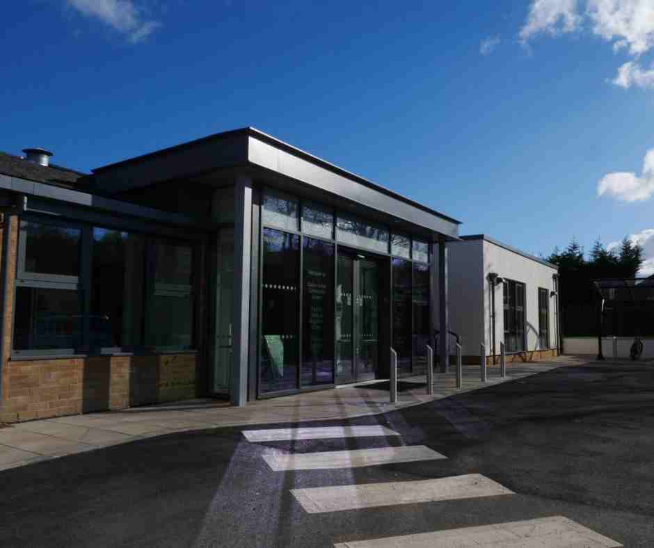 Modern community centre with glass entrance and brick walls under a clear blue sky