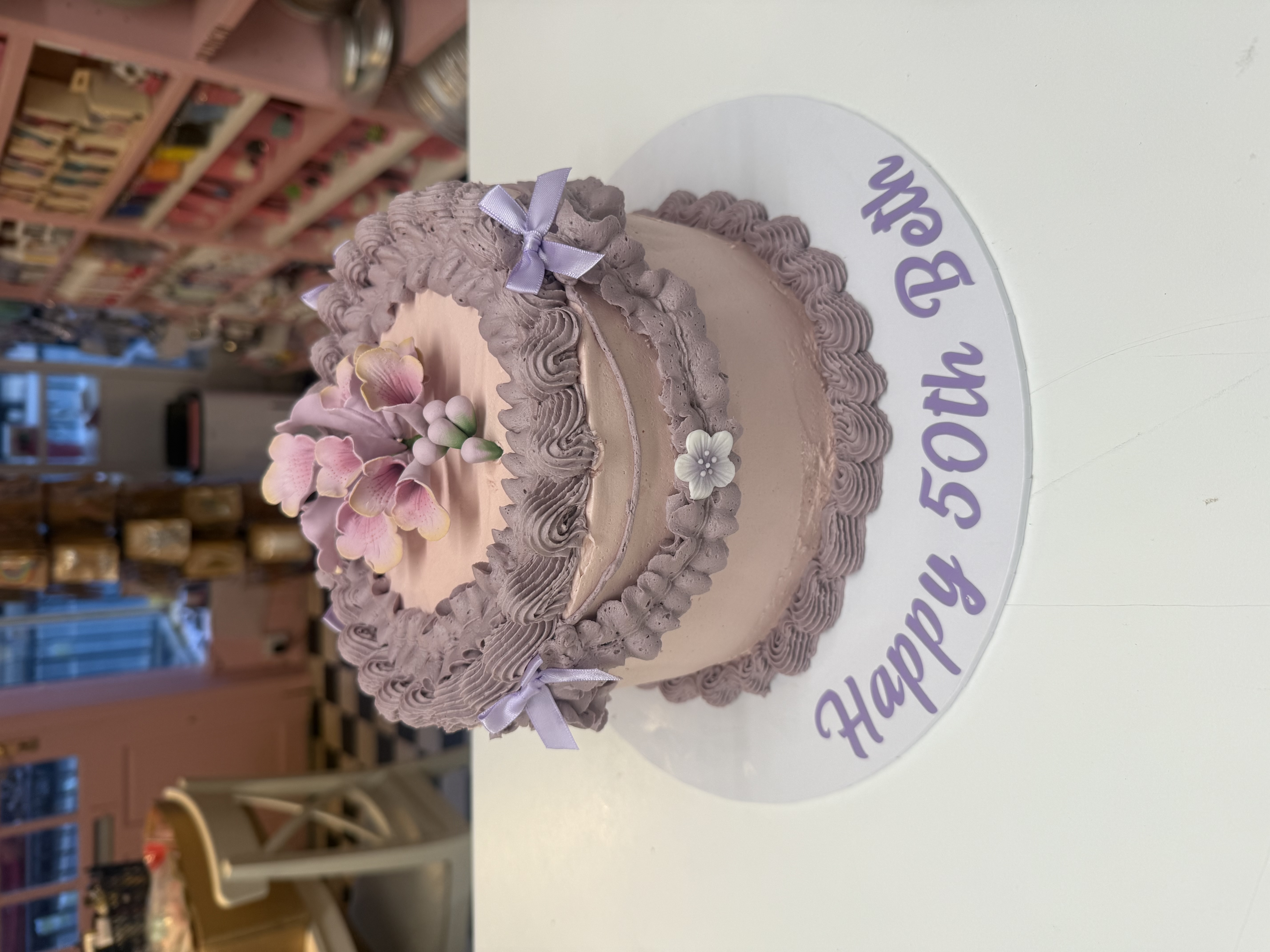 Elegant pink and purple birthday cake with floral decorations on a display counter
