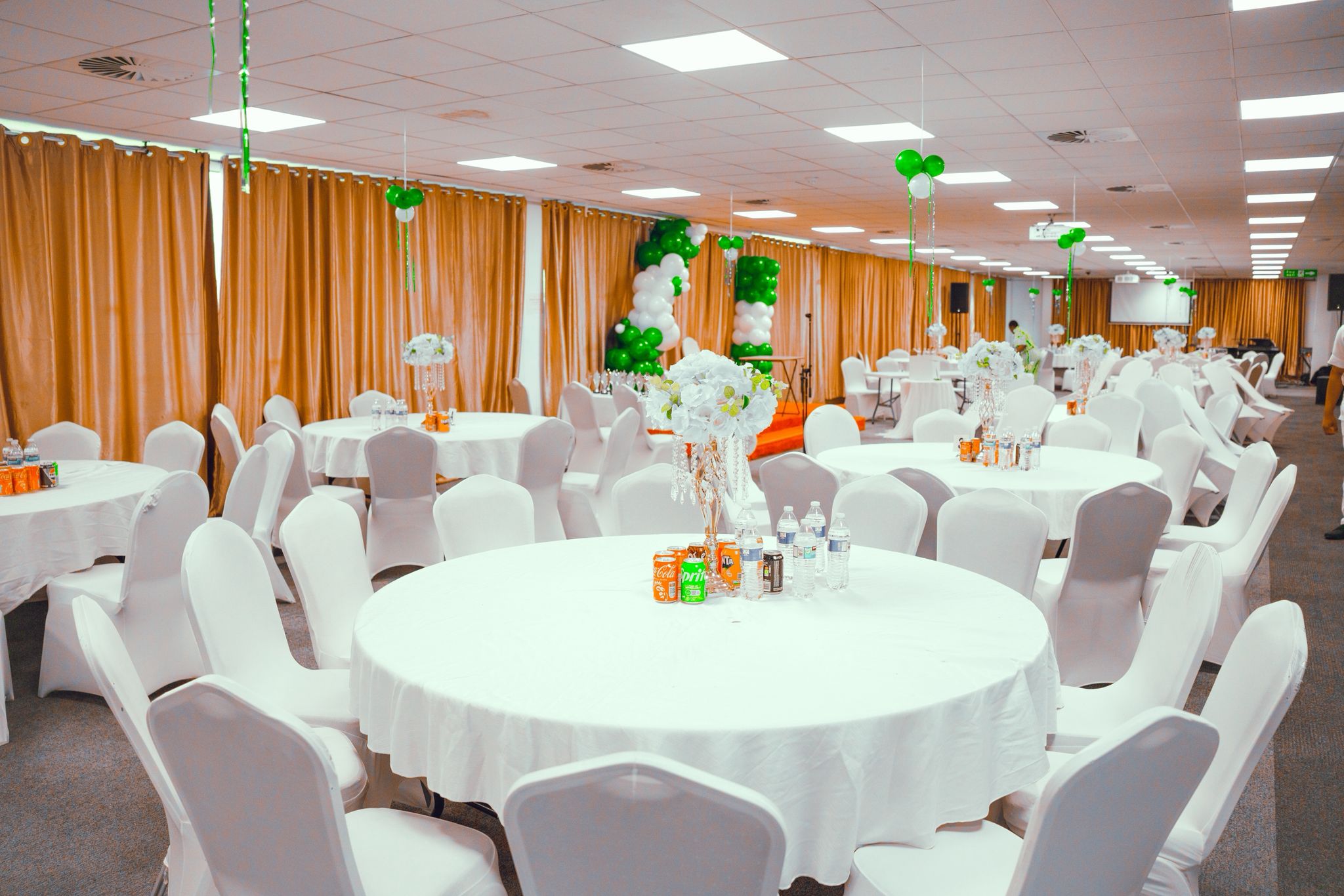 Spacious banquet hall with white tablecloths and green balloon decorations
