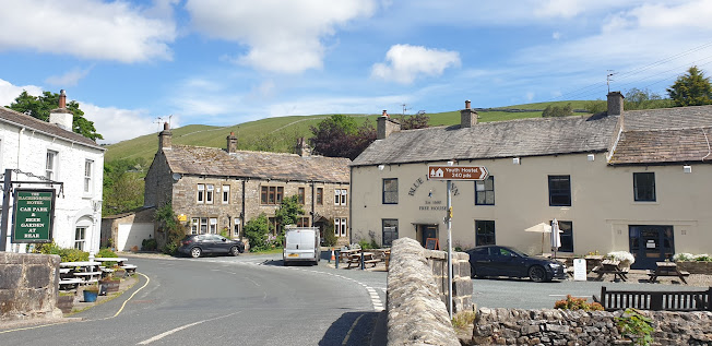 Charming Bed & Breakfast with stone buildings, outdoor seating, and scenic hills under a blue sky in Kettlewell, Yorkshire.