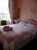 Cozy guest room with pastel decor, double bed, and folded towels on top. Large window with a view in Whitby, Yorkshire.