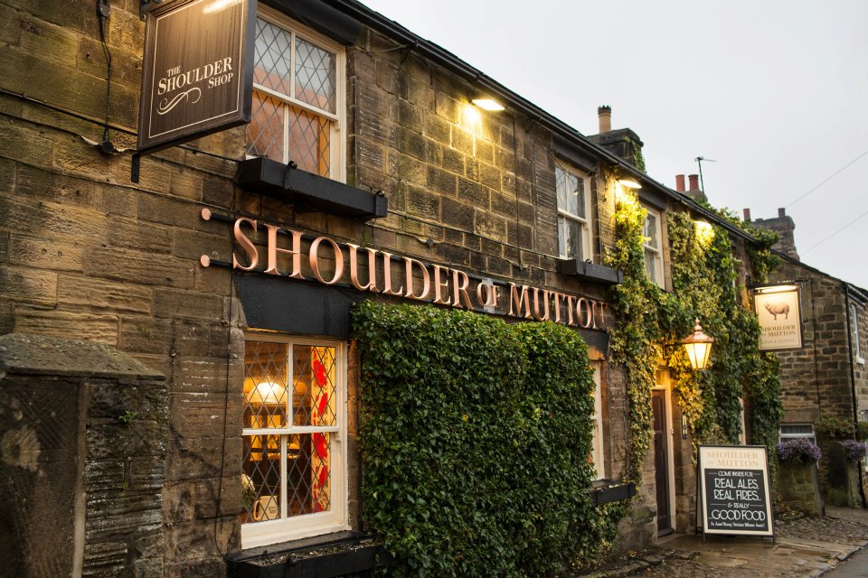 Traditional stone pub with ivy-covered walls, warm lighting, and signs for "Shoulder of Mutton" and local ales.