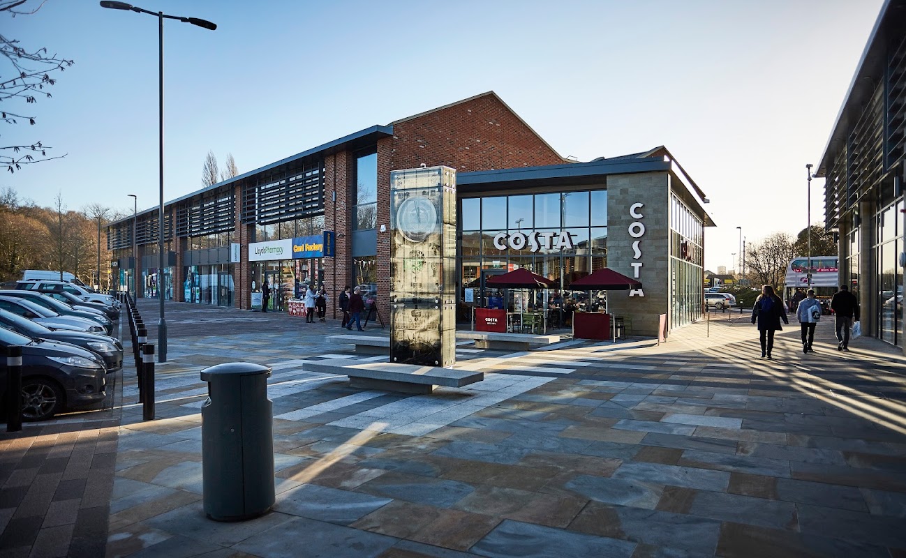Kirkstall Bridge Shopping Park featuring a Costa cafรฉ, shops, and parked cars under clear blue skies.