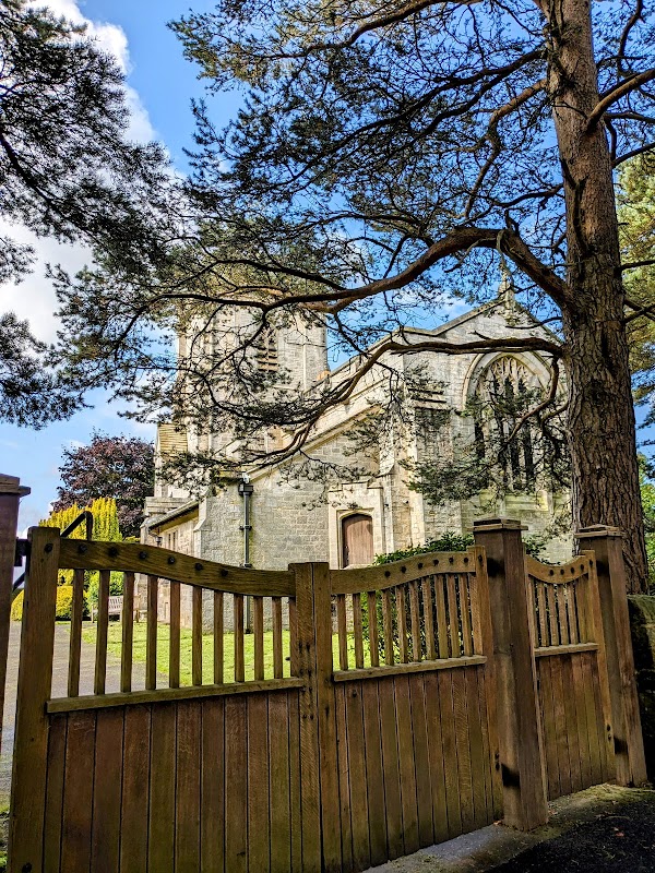 Winksley Banks Caravan & Lodge Park entrance with wooden gate, surrounded by trees and a stone building in the background.