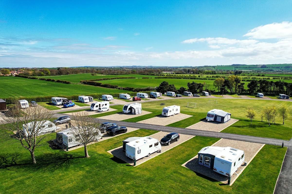 Caravan park with neatly arranged caravans on grassy plots, surrounded by green fields and blue sky in Lebberston, Yorkshire.