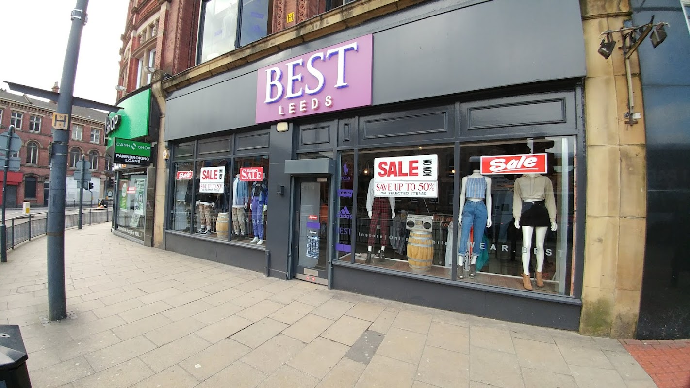 Corner shop "BEST" in Leeds with large sale signs, showcasing clothing displays and a modern storefront design.