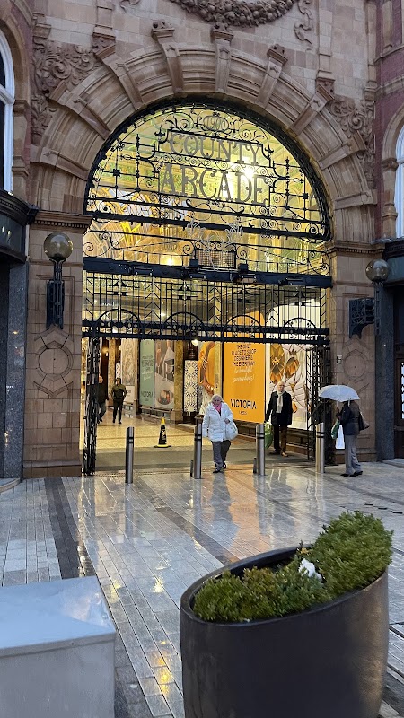 Entrance to County Arcade with ornate archway, shoppers, and wet pavement reflecting lights.